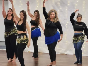 5 women dancing in black with blue fringe hip belts